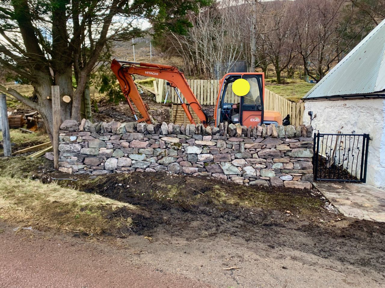 Newly built dry stone wall next to an old cottage in Annat, a digger in the background
