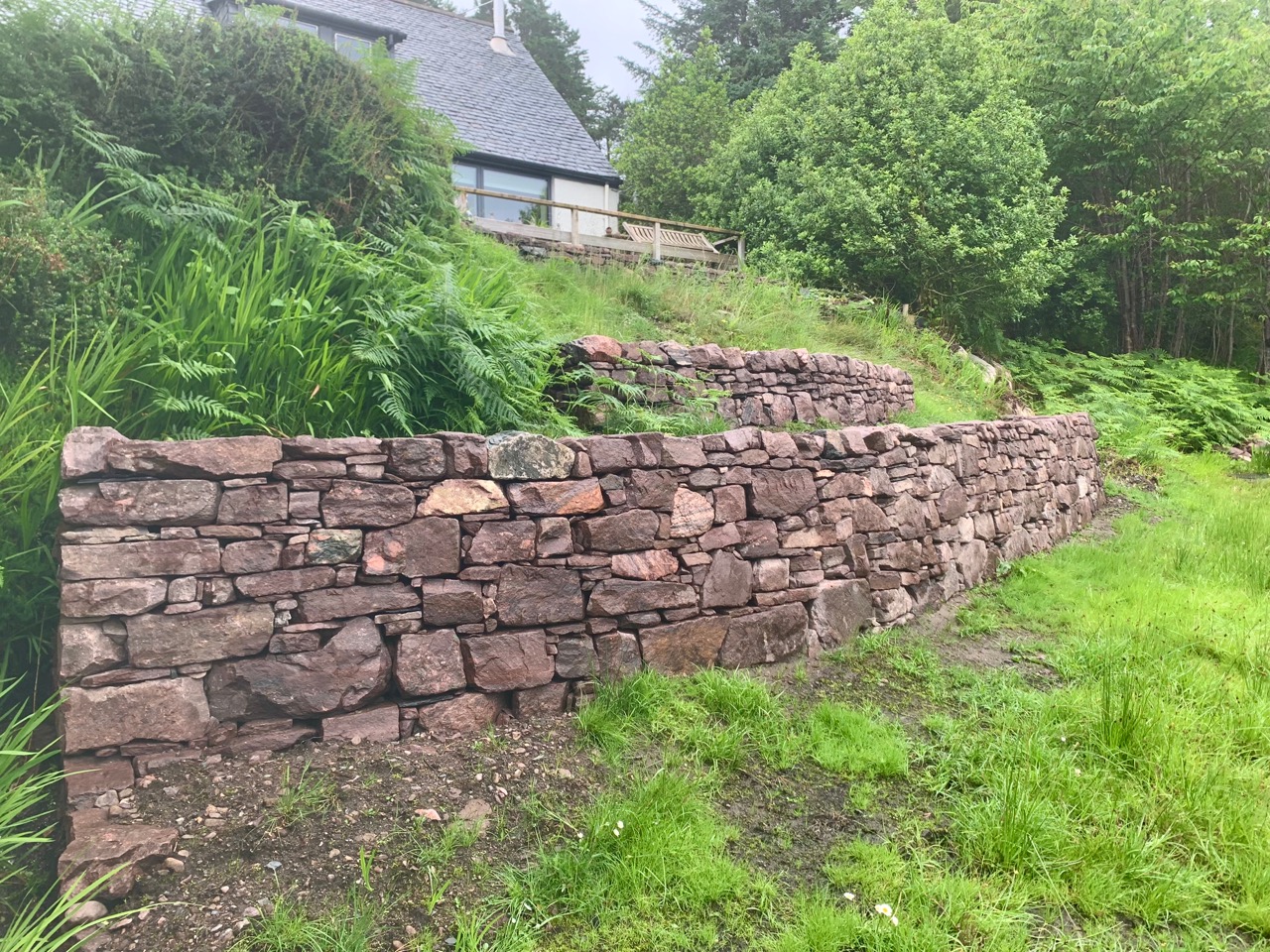 Three retaining walls built onto a grassy slope in terraces, the stone is pink.