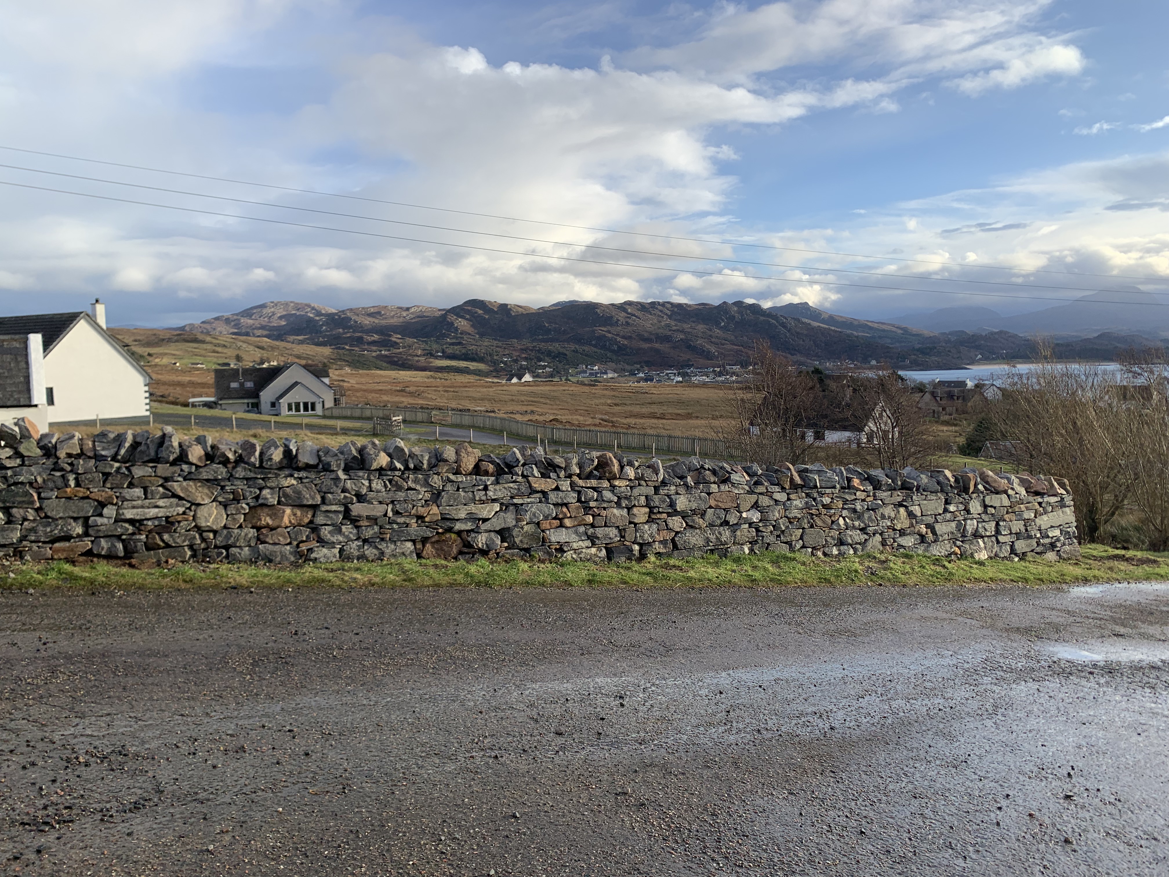 A newly built dry stone wall running down the side of a single track road with Gairloch village in the background