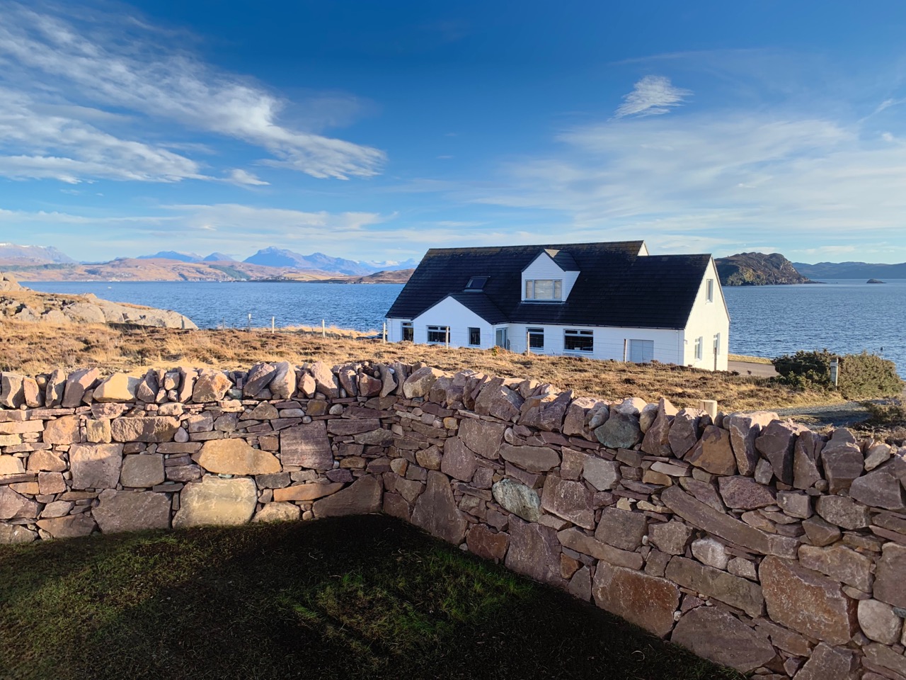 New built garden wall of pink torridonian sandstone in Mellon Charles with the sea and mountains in the background