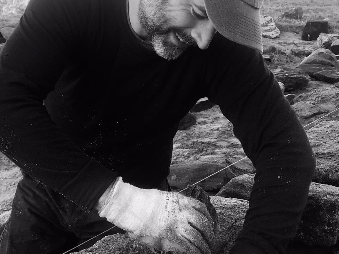 a dry stone waller wearing gloves placing a stone into a dry stone wall.
