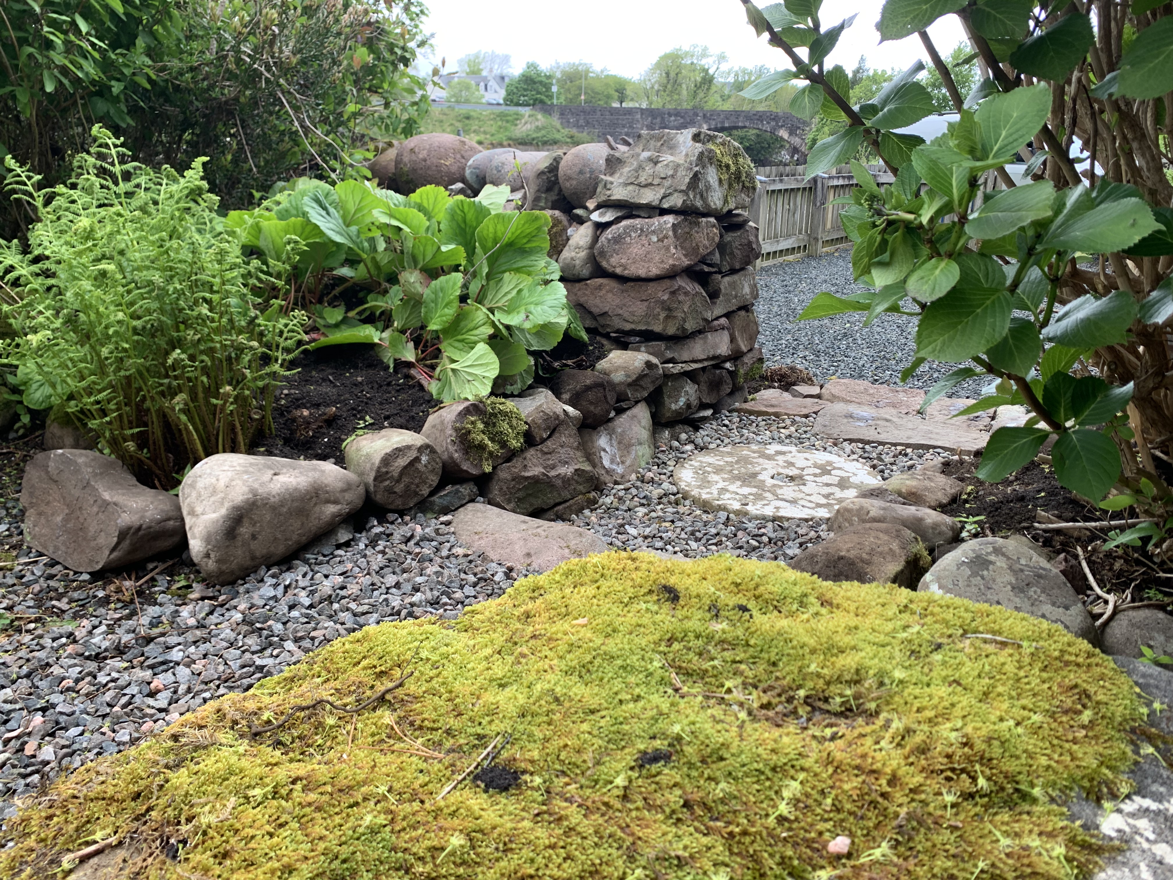 A short gravel path with stone insets and steps next to a raised bed and low dry stone wall.